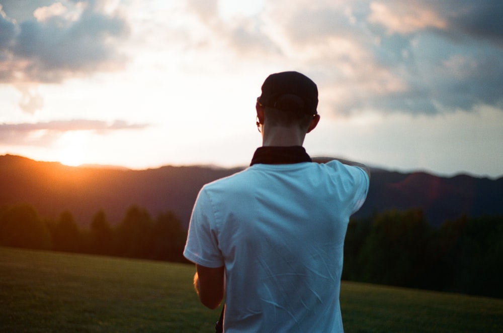 man in white crew neck t-shirt standing on green grass field during daytime