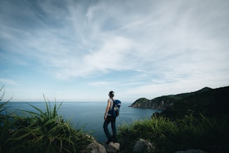 An elegant traveler with a backpack, standing on a cliff overlooking a vast jungle.