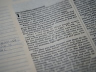 A close-up of a printed page from a book with text in columns. The text includes a header with a number and a small portion of handwritten notes is visible on a lined section on the left side.