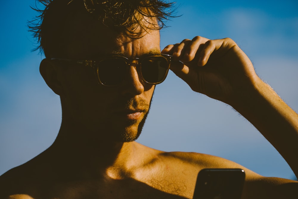 man wearing black sunglasses holding black smartphone during daytime