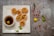 Five crispy puris filled with savory ingredients are placed on a square white plate. A small bowl of tangy water with a lemon slice floats nearby. Scattered around are a green chili, peanuts, a yellow lemon, and sprigs of coriander, creating a rustic presentation.