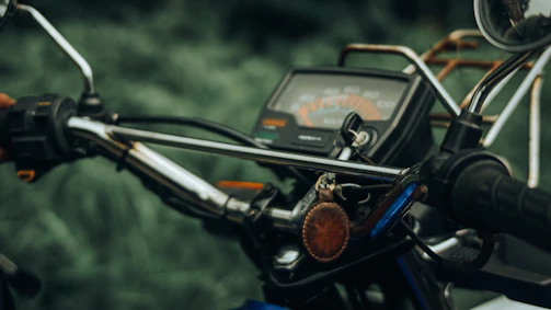 Close-up of a motorcycle's dashboard with glowing gauges and a leather-gloved hand gripping the handlebar.