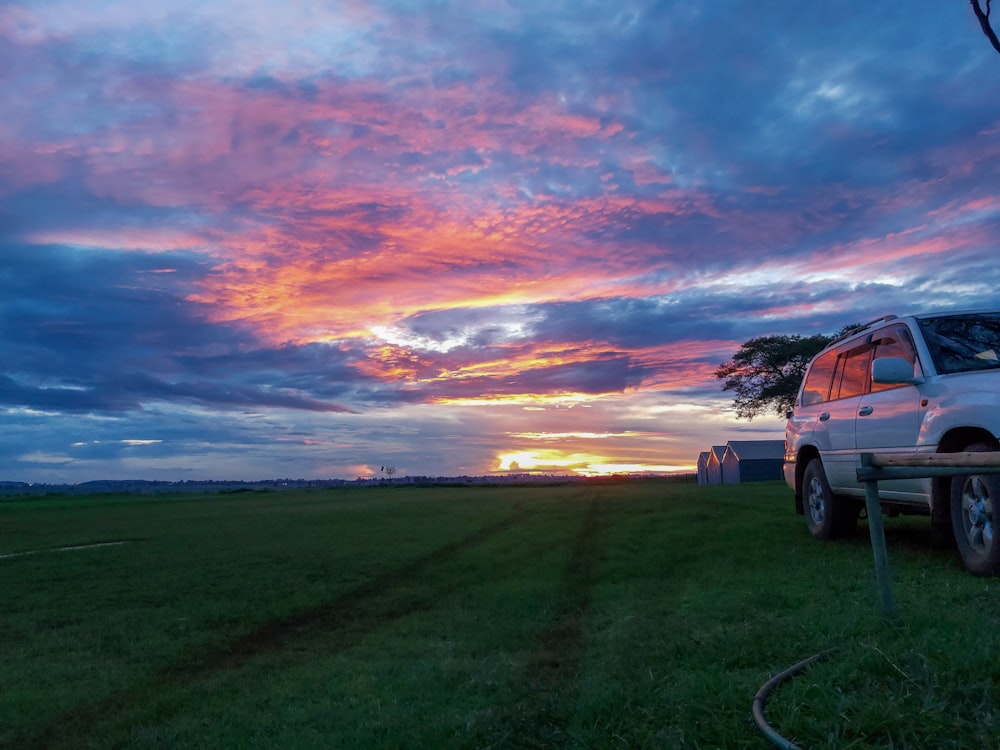 white suv on green grass field under cloudy sky during sunset