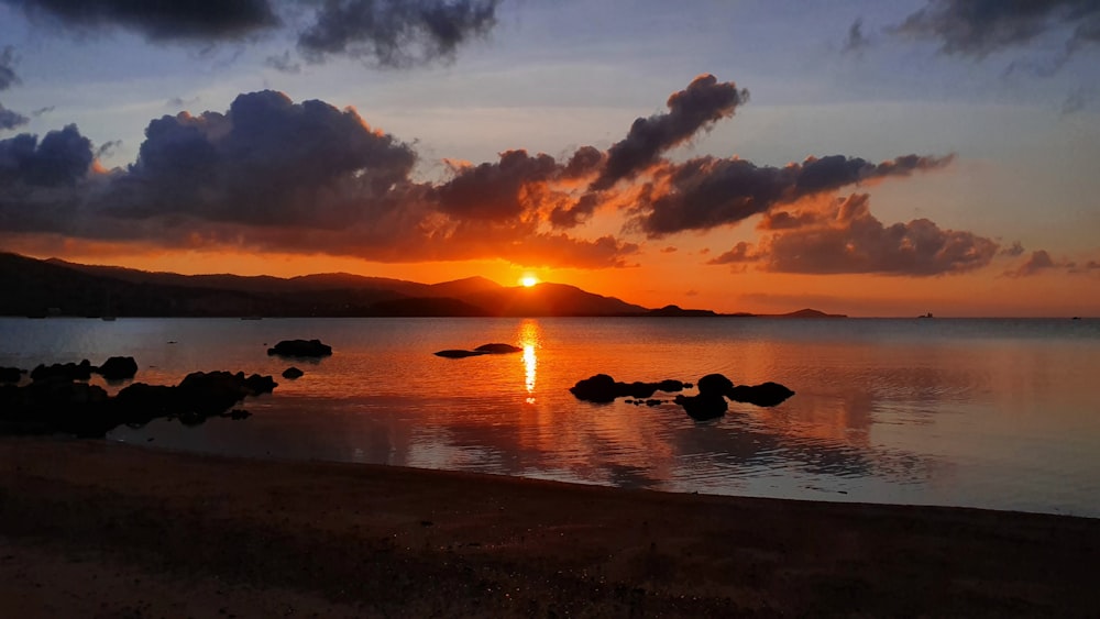 silhouette of rocks on sea shore during sunset