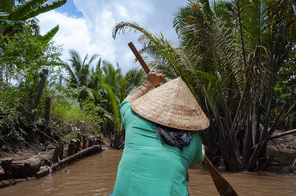 woman in green shirt and brown straw hat sitting on brown wooden dock during daytime