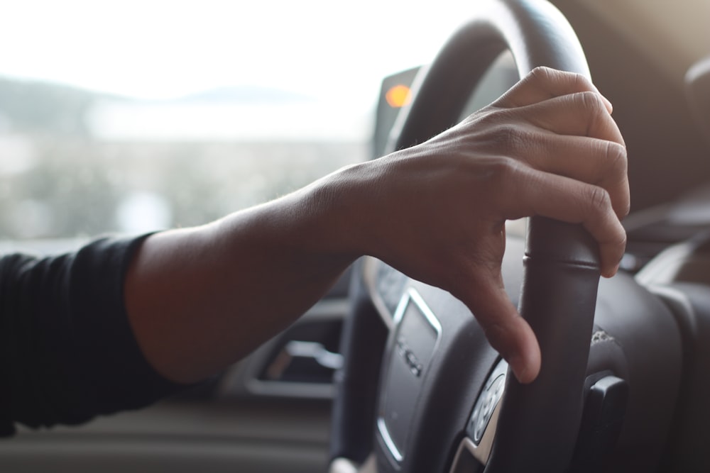 person holding black car steering wheel