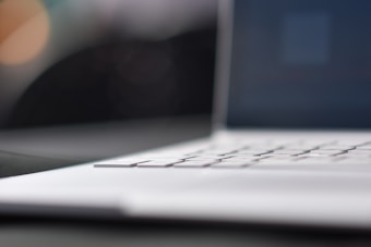 A close-up view of a laptop keyboard with a blurred screen in the background, suggesting an emphasis on the sleek design and keys of the device.