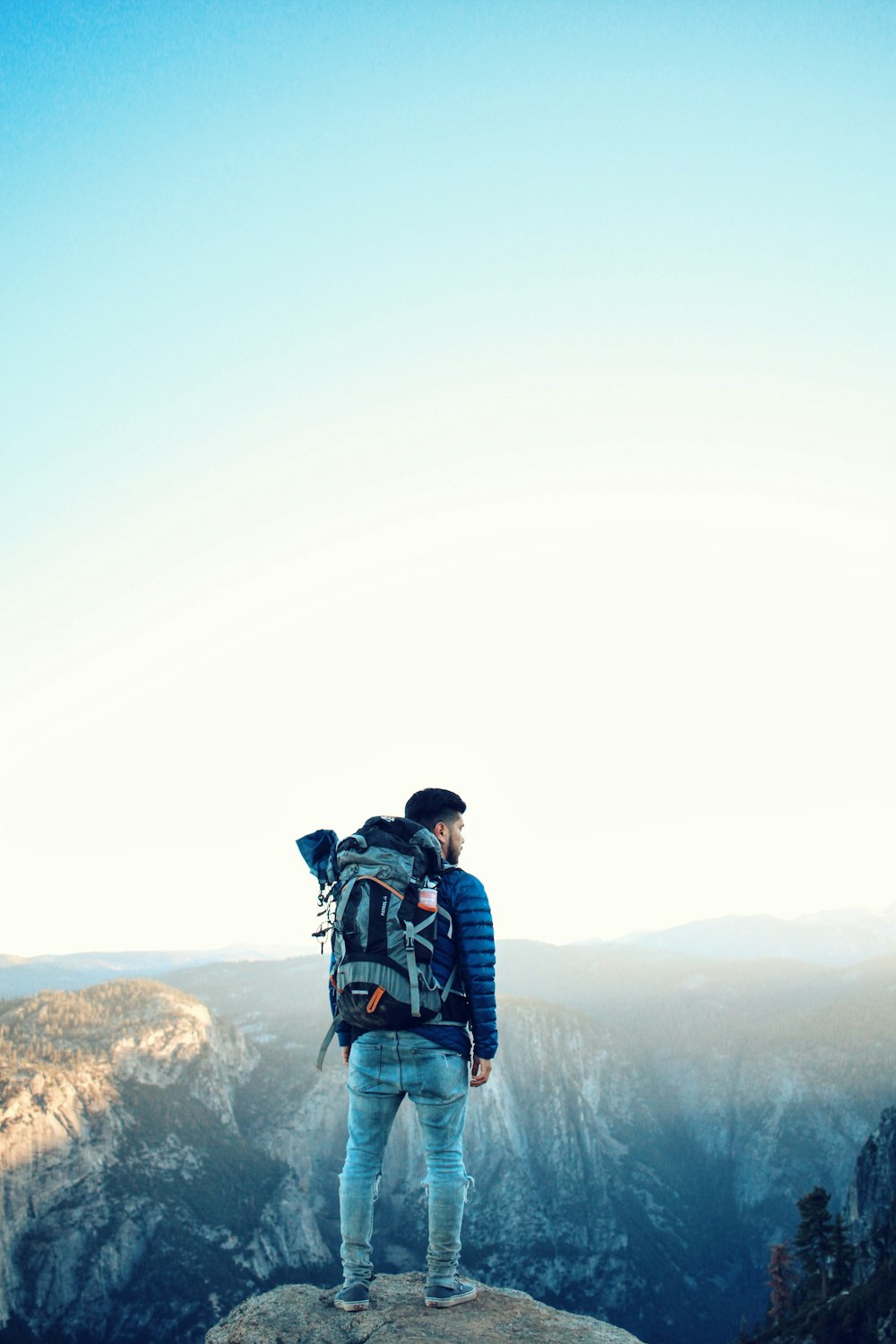 man in black and red jacket carrying black backpack standing on brown rock formation during daytime