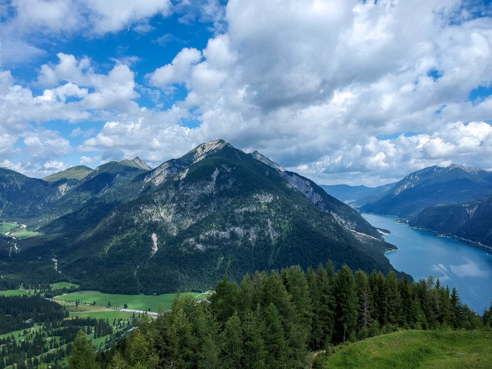 green trees near mountain under white clouds during daytime