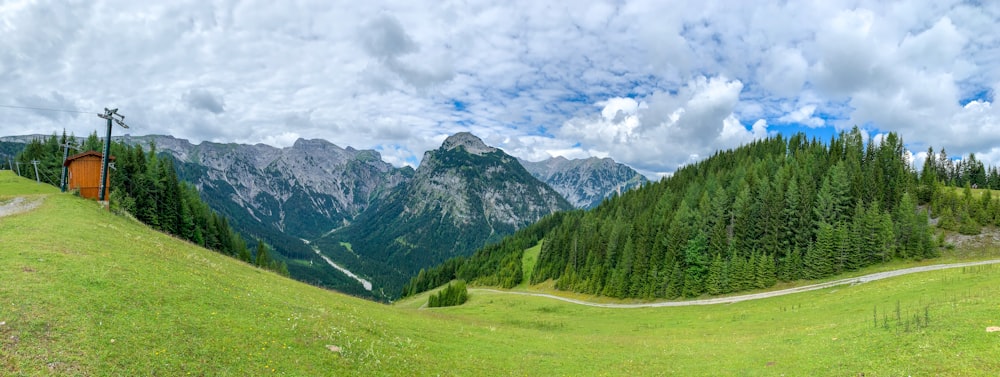 green grass field near green trees and mountains under white clouds during daytime