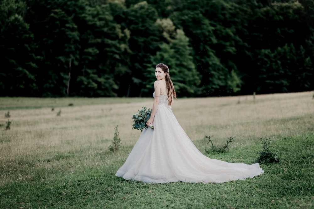 woman in white dress holding bouquet of flowers standing on green grass field during daytime