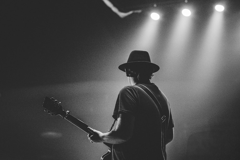 homem na camiseta preta e chapéu tocando guitarra