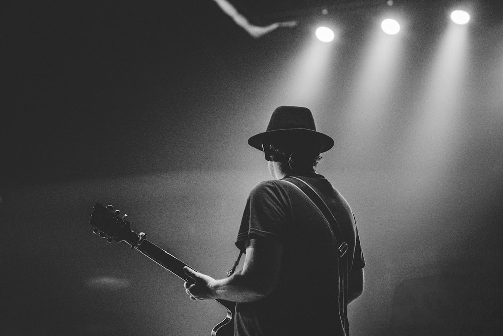 man in black t-shirt and hat playing guitar