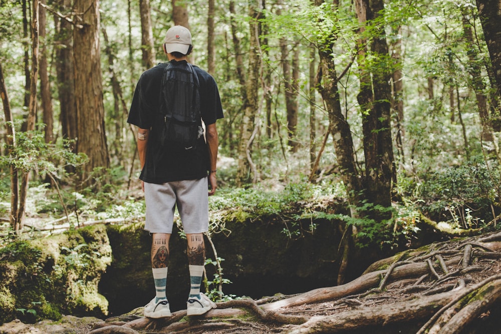 man in black jacket and white shorts standing on brown tree log during daytime