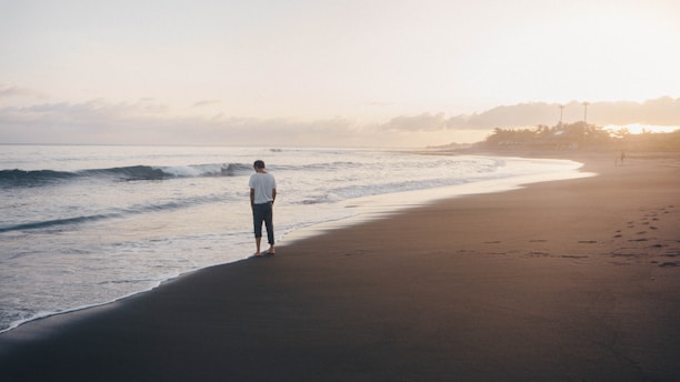 Person walking alone on beach at sunset, reflecting on trauma and healing