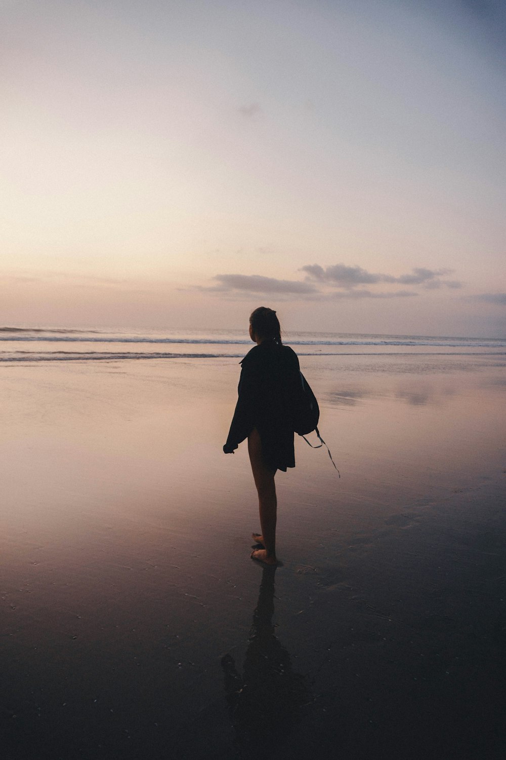 femme en manteau noir debout sur le bord de mer au coucher du soleil