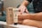 A person is applying hemp extract infused cream to their arm. The product is labeled with 1000mg full spectrum and is packaged in an eco-friendly paper box. The setting appears to be a comfortable indoor environment, with the individual seated on a couch.