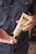 A person holds a tube of hemp extract-infused cream, dispensing a small amount into their other hand. The background is a blurred view of a person wearing a polka-dotted shirt.