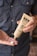 A person holds a tube of hemp extract-infused cream, dispensing a small amount into their other hand. The background is a blurred view of a person wearing a polka-dotted shirt.