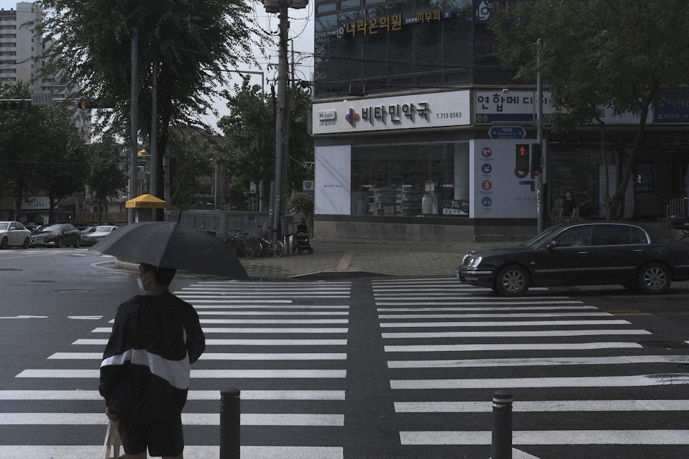 pessoa em jaqueta preta e branca segurando guarda-chuva andando na faixa de pedestres durante o dia