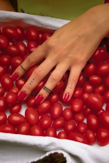 person with red manicure holding red tomato