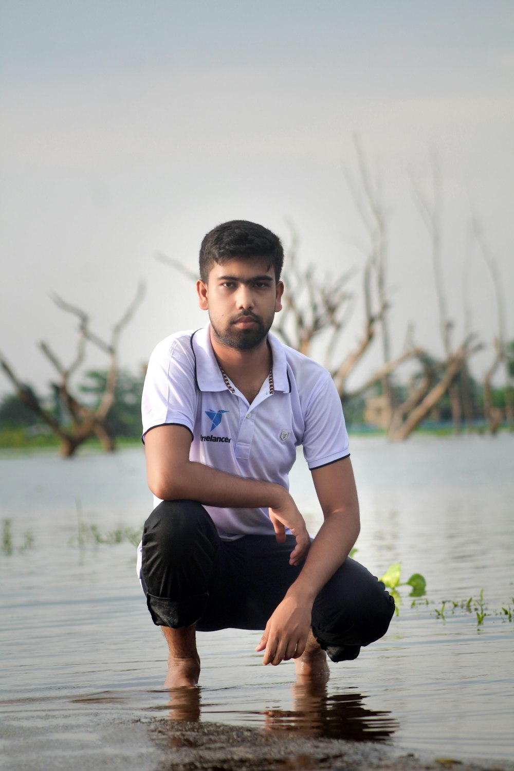 man in white polo shirt and black pants sitting on rock in lake during daytime