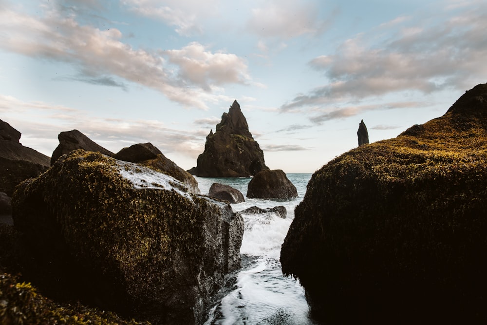 black rock formation on body of water under white clouds during daytime