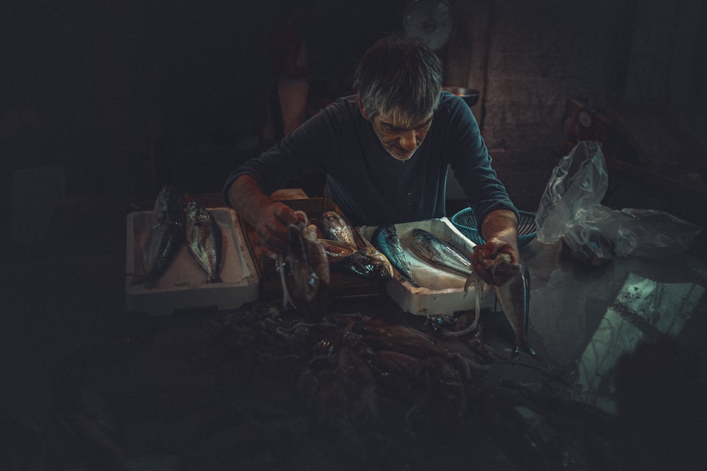 man in black long sleeve shirt holding knife slicing fish