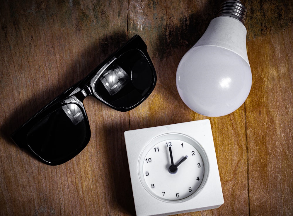 black framed sunglasses beside white round analog watch on brown wooden table