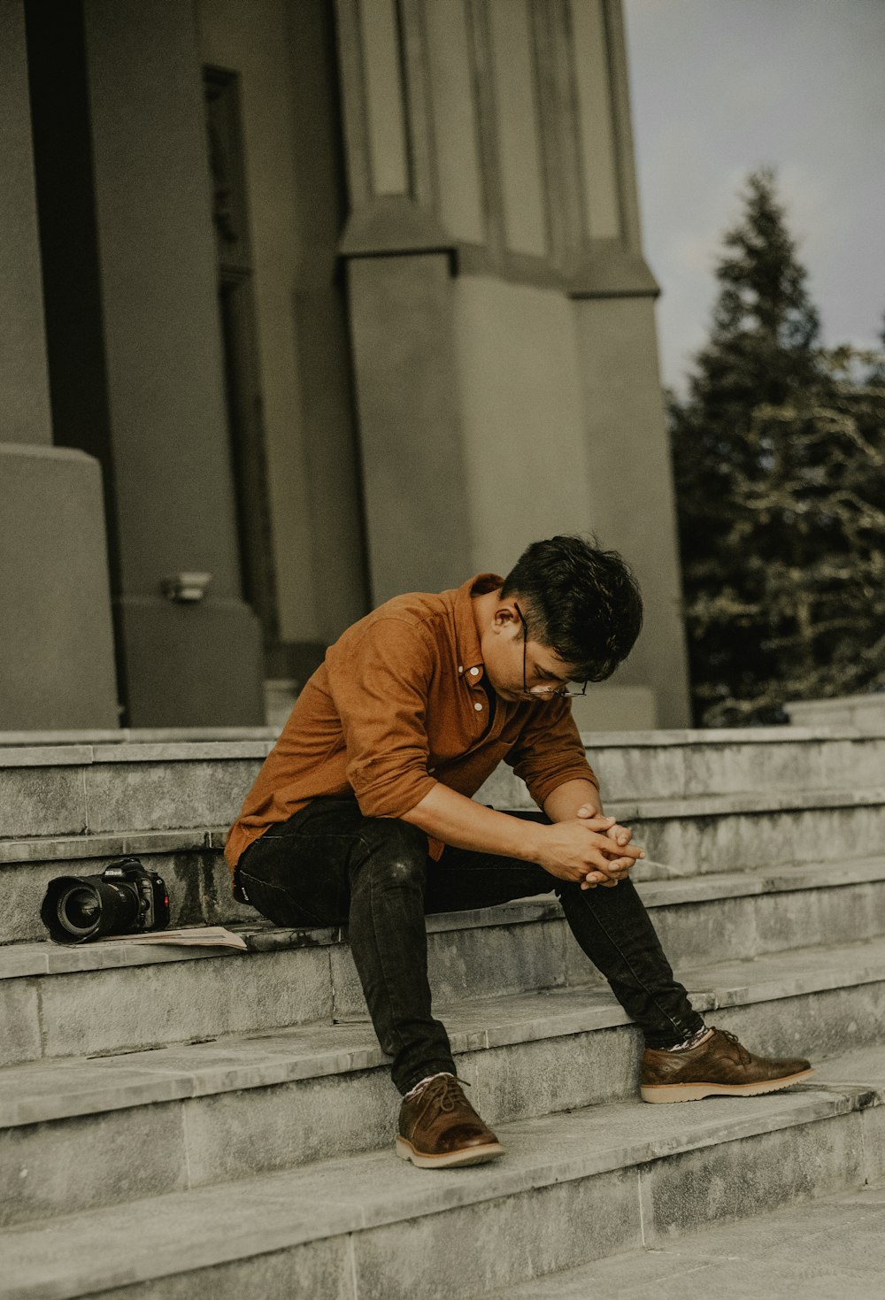 man in orange long sleeve shirt and black denim jeans sitting on concrete stair