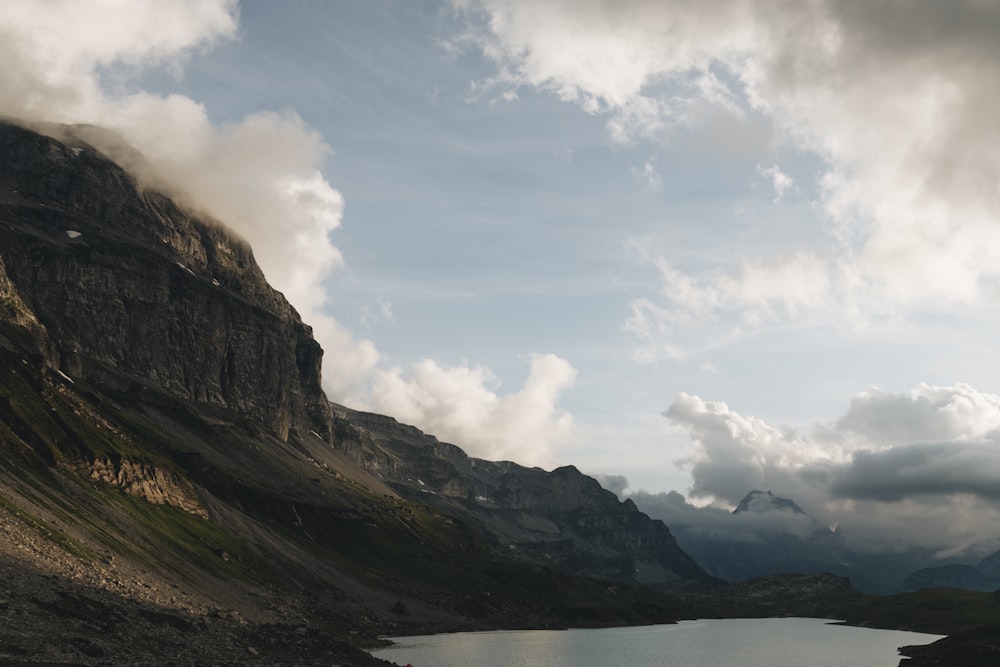 body of water near mountain under cloudy sky during daytime