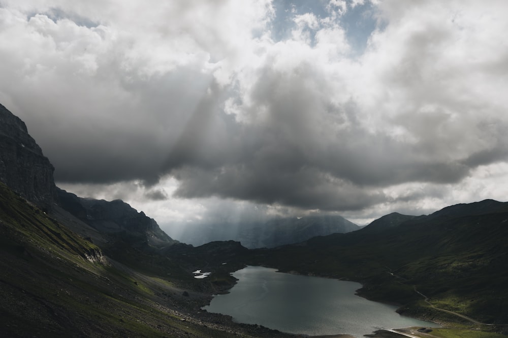 body of water near mountain under cloudy sky during daytime