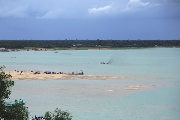 A serene riverside scene at Gangasagar with pilgrims gathered near the water under a soft saffron sky.