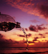 A chilled bottle of Awshal Water shining pink under the Omani sun by a flowing stream.