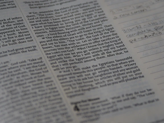 Close-up of a scholar's hands annotating a printed manuscript under warm library lighting.