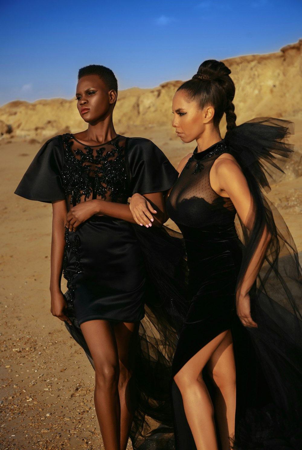 2 femmes en robe noire debout sur le sable brun pendant la journée
