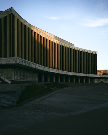 Evening view of a brutalist building illuminated softly, casting dramatic shadows that reveal its raw concrete texture.
