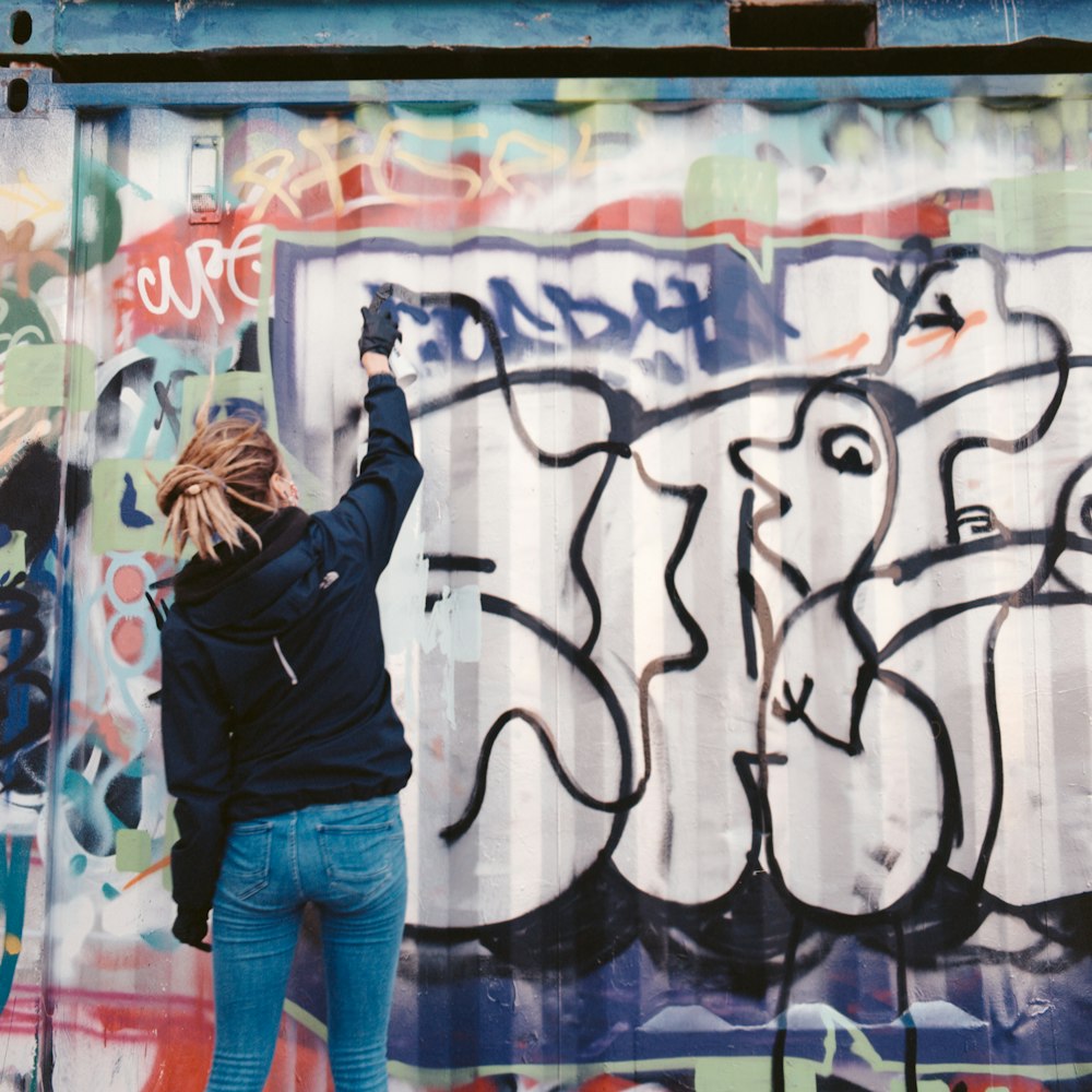 woman in black jacket and blue denim jeans standing in front of white and black wall