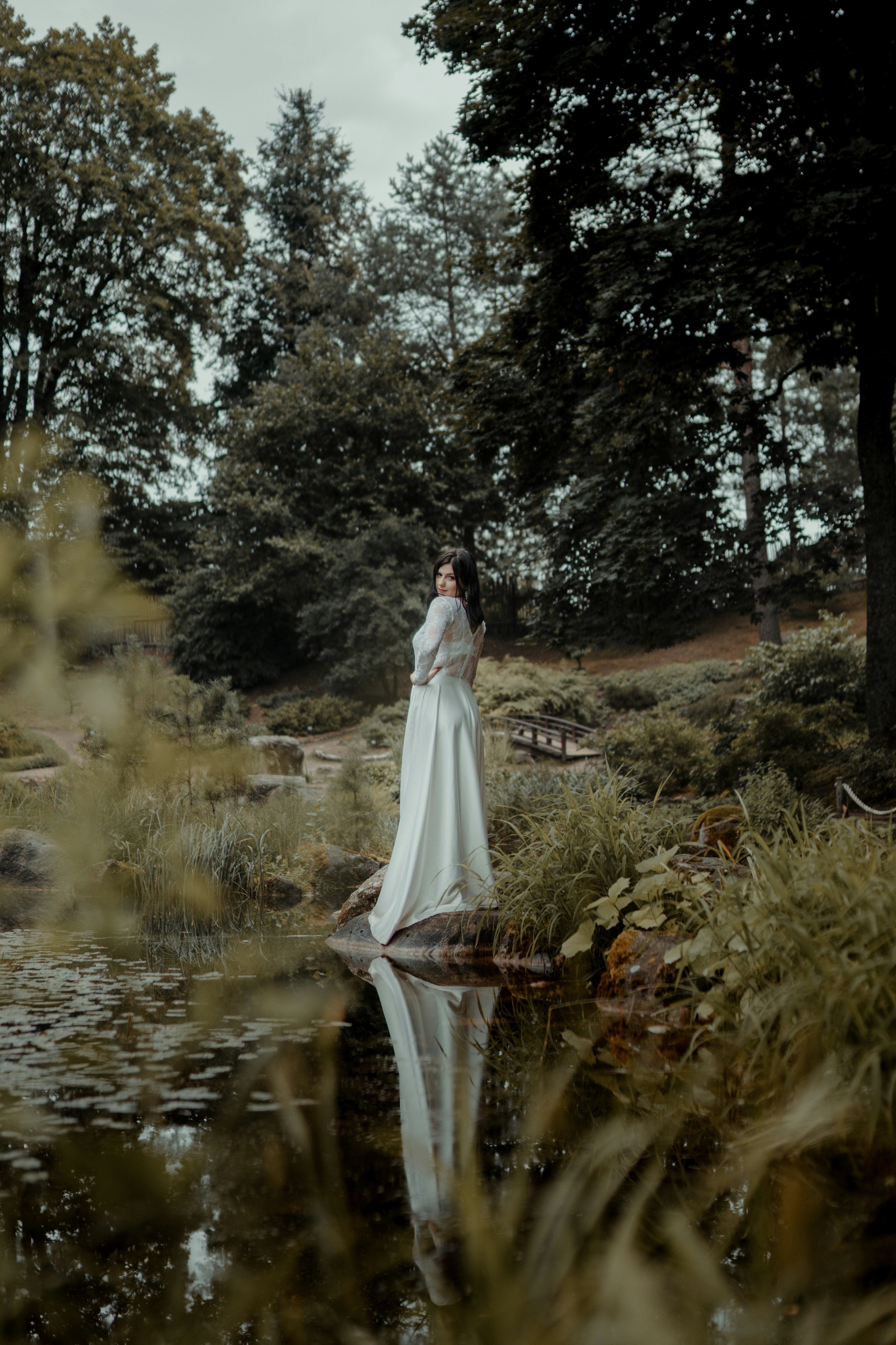 woman in white wedding dress standing on green grass field near river during daytime