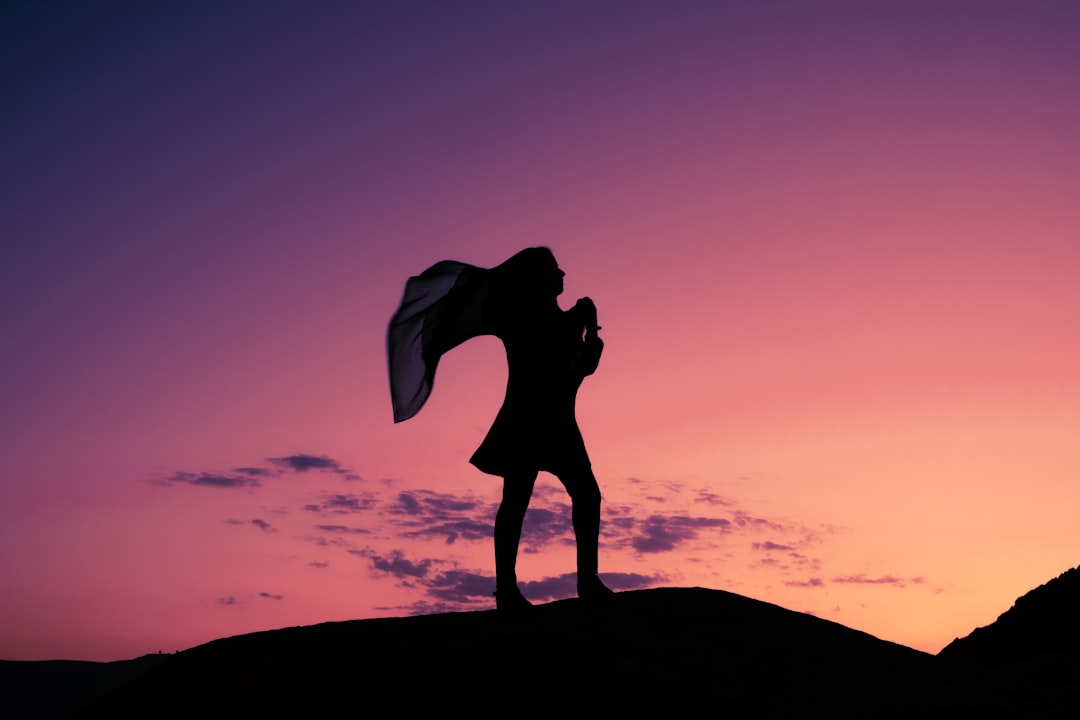silhouette of woman standing on rock during sunset