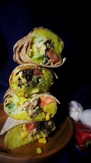 A stack of wrapped breakfast burritos ready for freezing, with a rustic kitchen background.