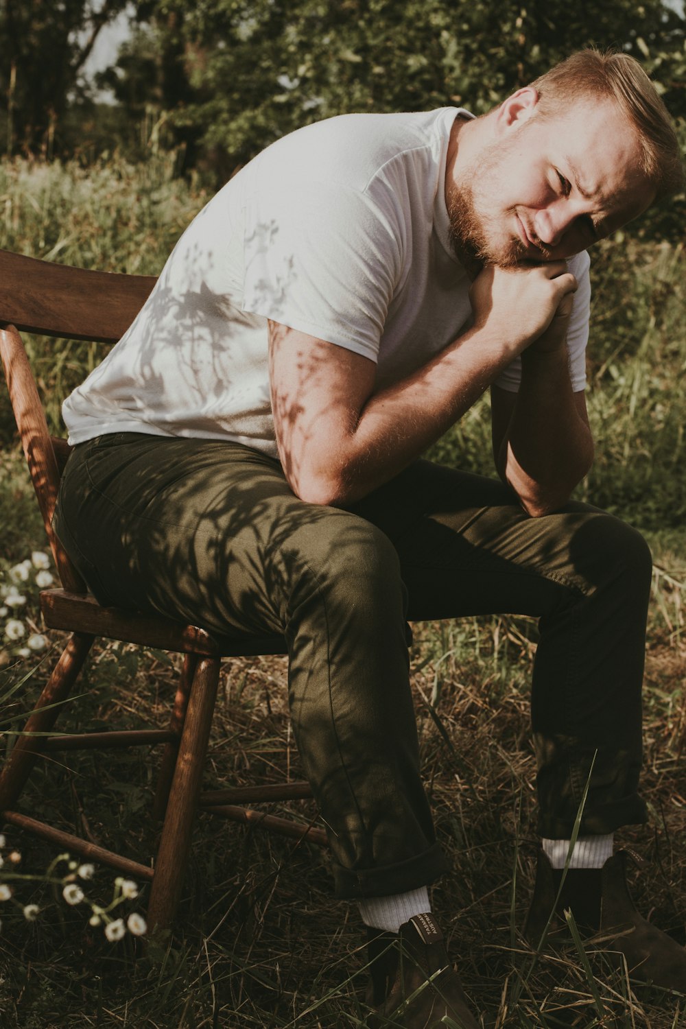 man in white t-shirt and brown pants sitting on brown wooden chair