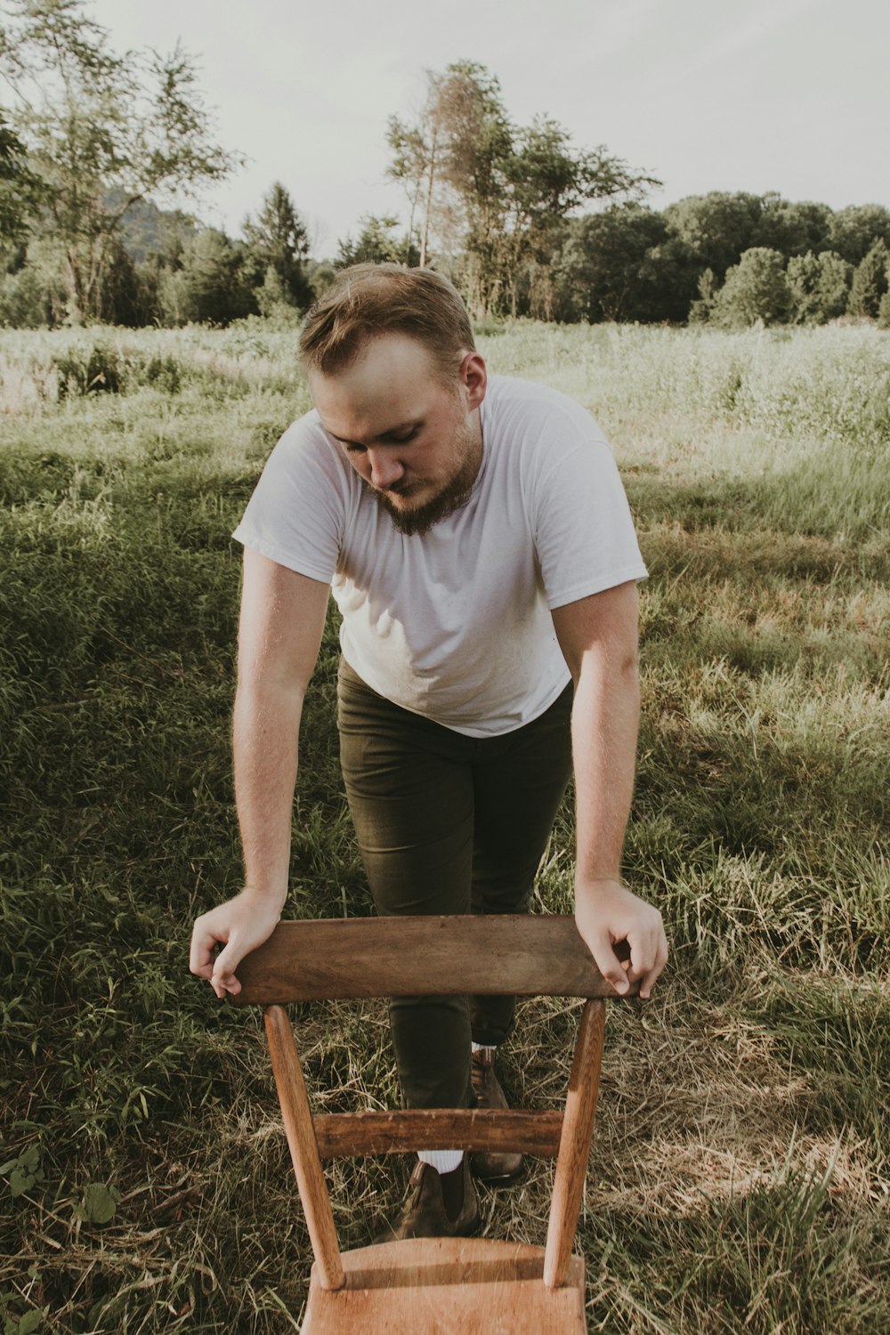 man in white crew neck t-shirt sitting on brown wooden chair during daytime