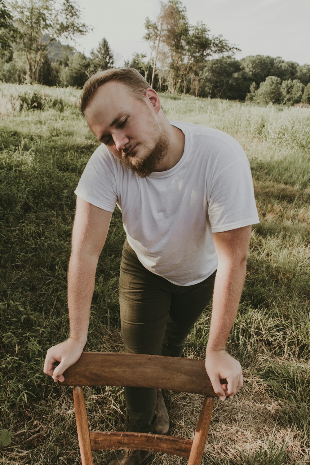 man in white crew neck t-shirt and gray pants sitting on green grass during daytime