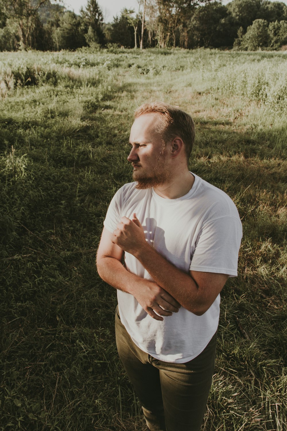 man in white crew neck t-shirt and brown pants sitting on green grass field during