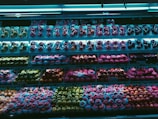 A supermarket fruit display showcases a wide variety of packaged fruits, including different types of apples and possibly other round fruits, arranged neatly across multiple shelves. The lighting casts a blue hue over the scene, highlighting the vibrant colors of the fruits.