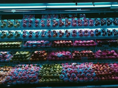 A supermarket fruit display showcases a wide variety of packaged fruits, including different types of apples and possibly other round fruits, arranged neatly across multiple shelves. The lighting casts a blue hue over the scene, highlighting the vibrant colors of the fruits.