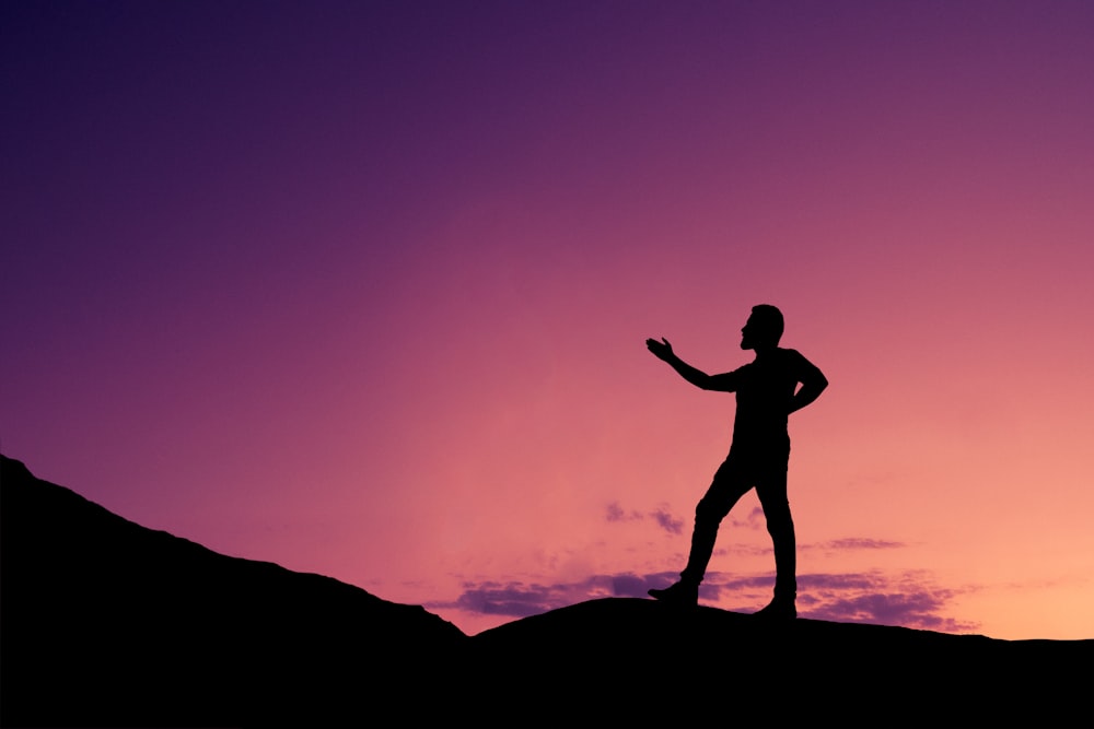 silhouette of man standing on rock during sunset