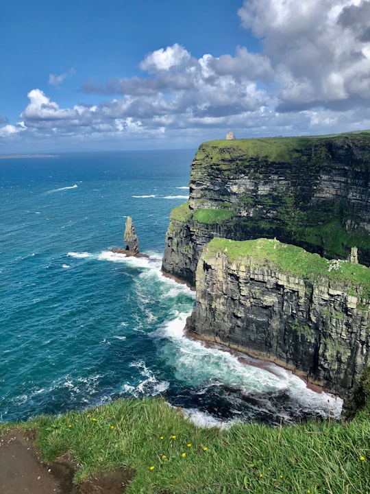 green and gray rock formation beside blue sea under blue sky during daytime in Cliffs of Moher Ireland
