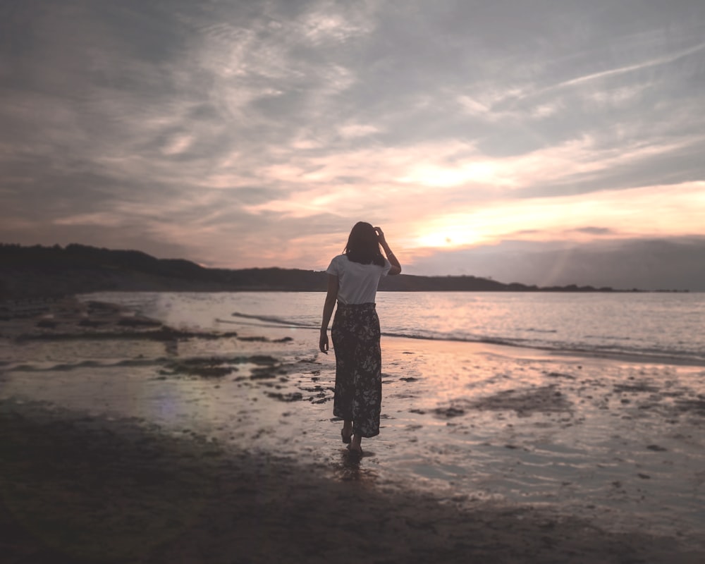Frau in weißem Tanktop und schwarzem Rock steht bei Sonnenuntergang am Strand